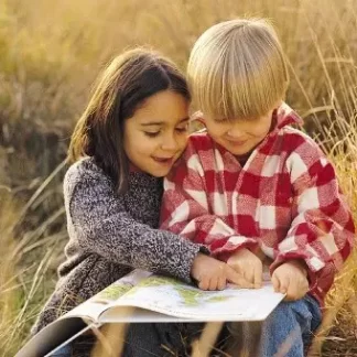 Produktbild zu Persönliches Kinderhoroskop: Ein Junge und ein Mädchen sitzen in einem Feld und schmökern in einem Atlas